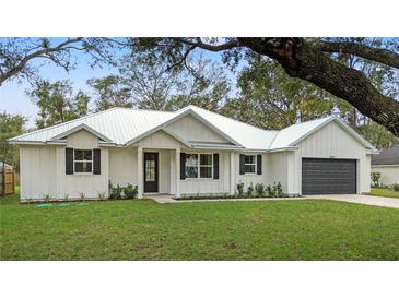White farmhouse exterior boasts metal roof, shutters, and landscaping at 18315 Dells Cv, Groveland, FL 34736