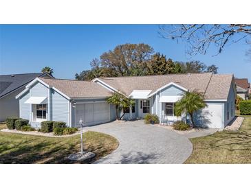 Charming light blue home featuring a circular paved driveway, well-manicured lawn, and mature landscaping at 1001 Del Rio Dr, The Villages, FL 32159