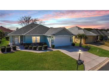 Charming home with a well-manicured lawn, lush landscaping, and a two-car garage at sunset at 8660 Se 132Nd Ln, Summerfield, FL 34491