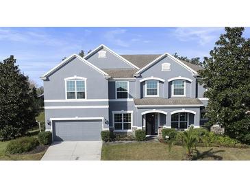 Charming two-story home featuring a well-manicured lawn, gray stucco, an attached garage, and tastefully designed architecture at 887 Daisy Hill Ct, Apopka, FL 32712