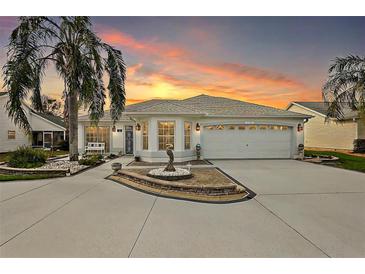 Beautiful home featuring a well-manicured front yard, fountain, and two-car garage as the sun sets at 1508 Dellano Way, The Villages, FL 32159