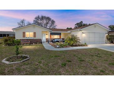 Charming home featuring a well-maintained front yard, a covered porch area, and a two-car garage at 17764 Se 95Th Ct, Summerfield, FL 34491