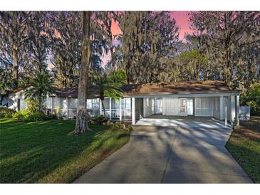 Charming single-story home featuring a screened-in porch and convenient carport with lush landscaping and mature trees at 11243 Dead River Rd, Tavares, FL 32778