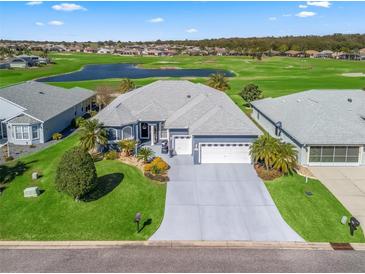 Well-maintained blue home with a three-car garage, lush lawn, and manicured landscaping overlooking a golf course and pond at 12390 Se 176Th Loop, Summerfield, FL 34491