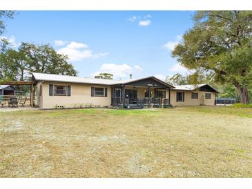 Tan home featuring a metal roof, a porch with black trim, and a large front yard with mature trees at 14100 Ne 46Th St, Silver Springs, FL 34488