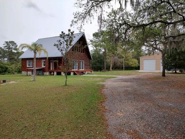 Rustic cabin home with a metal roof, stone foundation, and a large yard with mature trees and detached garage at 14415 County Road 448, Tavares, FL 32778