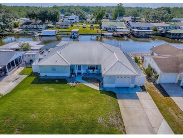 Waterfront single-story home with a metal roof, green lawn and a boat dock and lift on a canal at 26608 E Cove Dr, Tavares, FL 32778
