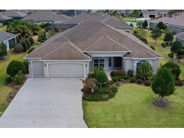 Well-maintained single-story home featuring an attached three-car garage, manicured lawn, and mature landscaping at 2935 Cedar Grove Loop, The Villages, FL 32163