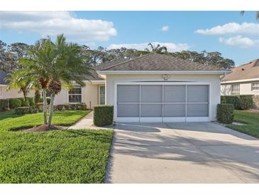 Charming single-story home with a well-manicured lawn, lush landscaping, and a screened two-car garage at 592 Juniper Way, Tavares, FL 32778