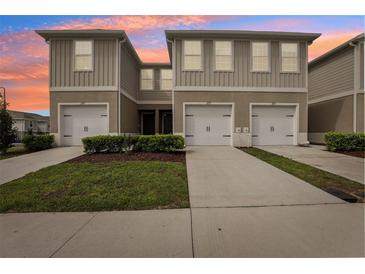 Modern townhomes with attached garages, concrete driveways, and manicured landscaping against a colorful sky at 255 Blueberry Ln, Davenport, FL 33837
