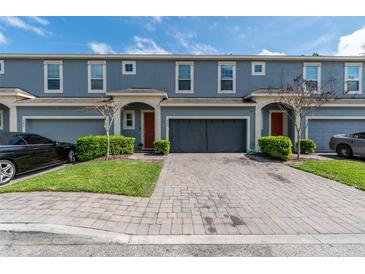 Exterior view of blue townhomes featuring a paver driveway, garages, manicured landscaping and red front doors at 384 Coral Beach Cir, Casselberry, FL 32707