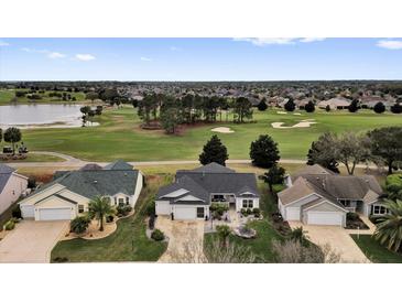 An aerial view of a well-manicured lawn and landscaping for multiple homes overlooking a golf course and pond at 1755 Lakewood Dr, The Villages, FL 32162