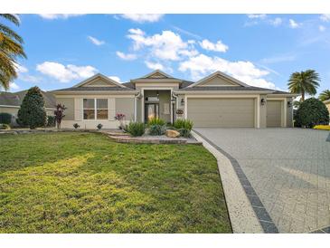 Charming single-story home with lush landscaping, a brick-paved driveway, and a well-manicured front lawn at 2882 Adrienne Way, The Villages, FL 32163