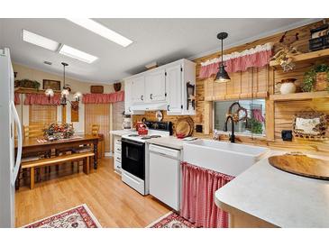 Quaint kitchen featuring skylights, wood paneling, white appliances and white cabinets at 313 Westwood Dr, Leesburg, FL 34748