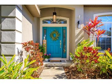 Inviting front entrance with a bright teal door, decorative wreath, transom window and colorful landscaping at 519 Hearthglen Blvd, Winter Garden, FL 34787