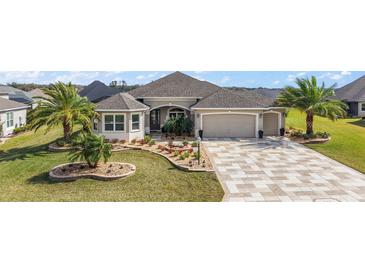 Well-manicured home exterior featuring a two-car garage, lush landscaping, and a paver driveway at 712 Krietemeyer Path, The Villages, FL 32163