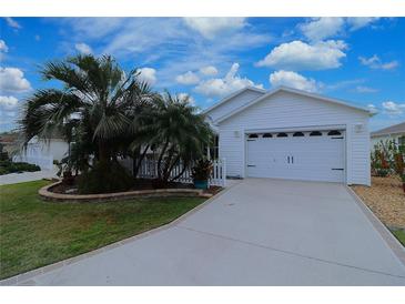 Charming single-story home featuring a two-car garage, a well-manicured lawn, and tropical landscaping at 1808 Endsley Ct, The Villages, FL 32162