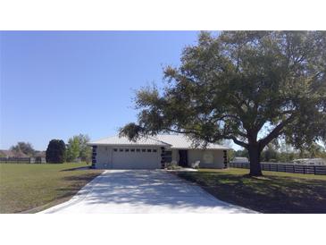 Charming single-story home with a metal roof, well-manicured lawn, and an attached two-car garage at 9265 County Road 128C, Wildwood, FL 34785