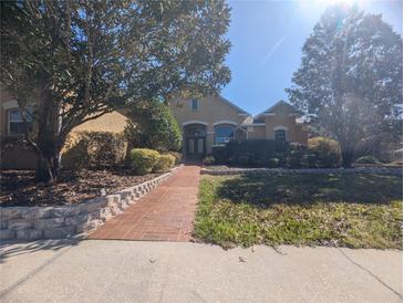 Inviting front exterior of a tan two-story home with mature trees and a brick walkway at 42316 E Saffron Ct, Eustis, FL 32736