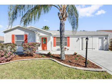 Charming single-story home featuring a well-manicured lawn, front-facing garage and a welcoming red front door at 9511 Se 168Th Elderberry Pl, The Villages, FL 32162