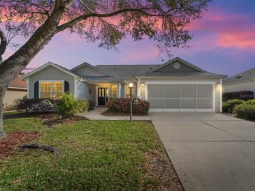 Charming single-story home featuring a well-maintained lawn, mature landscaping and a two-car garage at sunset at 17635 Se 82Nd Annadale Ter, The Villages, FL 32162