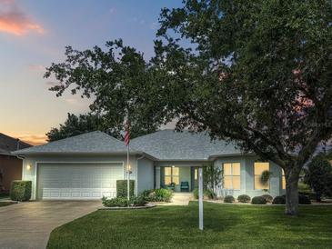 Charming single-story home with a well-manicured lawn, mature tree, and a two-car garage at dusk at 26821 Augusta Springs Cir, Leesburg, FL 34748