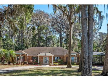 Charming brick home featuring mature trees and a well-manicured front lawn and circular driveway at 11215 Dead River Rd, Tavares, FL 32778
