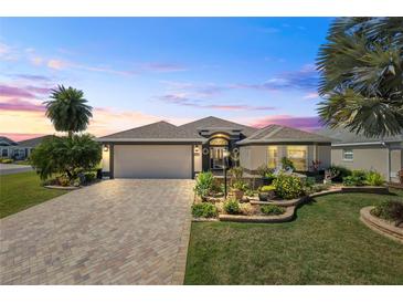 Beautiful single-story home featuring a well-manicured lawn, lush landscaping and a paver driveway at 2947 Rain Lily Loop, The Villages, FL 32163