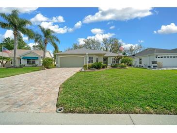 Charming home featuring a lush green lawn, mature palm trees, and a brick paver driveway under a blue sky at 2413 Tamarindo Dr, The Villages, FL 32162