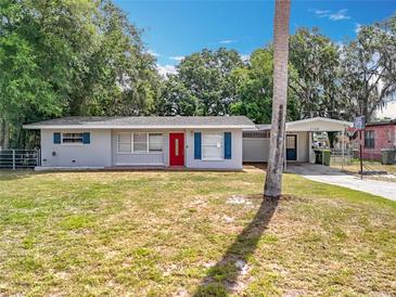 Charming single-story home featuring a bright red front door, manicured lawn, and covered carport at 1108 Cedar St, Leesburg, FL 34748