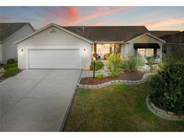 Charming single-story home boasts manicured landscaping, a two-car garage and cozy front porch at sunset at 16721 Se 77Th Northridge Ct, The Villages, FL 32162