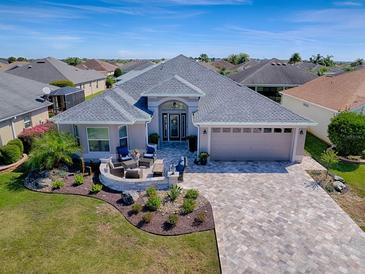 Stunning home featuring a lush front lawn, paver driveway, and a cozy fire pit area for outdoor relaxation at 2922 Rain Lily Loop, The Villages, FL 32163