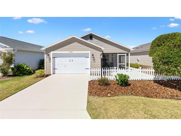 Charming single-story home featuring a white picket fence, well-manicured lawn, and attached two-car garage at 1773 Hallandale Ln, The Villages, FL 32162