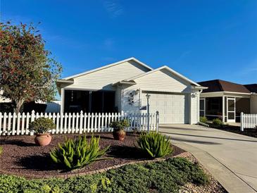 Charming single-story home with a well-manicured lawn, white picket fence, and attached garage at 2569 Errol Ter, The Villages, FL 32162