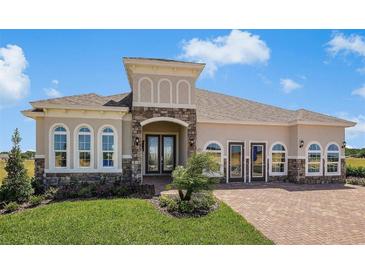 Stunning single-story home with stone accents, arched windows, and meticulously landscaped front yard with brick-paved driveway at 2408 Juniper Berry Dr, Minneola, FL 34715