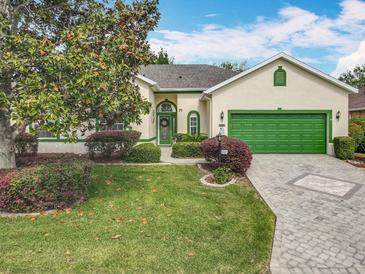 Charming single-story home with lush landscaping, a green two-car garage door, and a brick driveway at 24112 Robinwood St, Leesburg, FL 34748