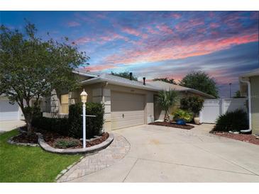 Charming home featuring a beige exterior, lush landscaping, and an attached two-car garage at 1135 Easley Way, The Villages, FL 32162
