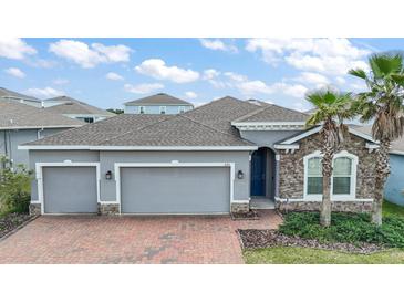 Charming single-Gathering home with three-car garage, stone accents, brick-paved driveway, and well-manicured landscaping at 3193 Hill Point St, Minneola, FL 34715