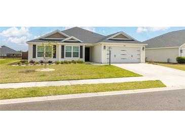 Charming single-story home with well-manicured lawn, lush landscaping, and an attached two-car garage at 3273 Dzuro Dr, Oxford, FL 34484