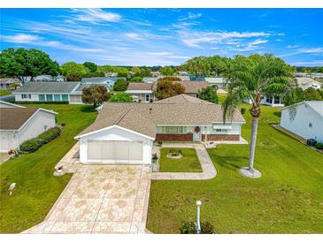 Charming home featuring a manicured lawn, palm tree, patterned driveway, and an attached two-car garage at 9773 Se 179Th Pl, Summerfield, FL 34491