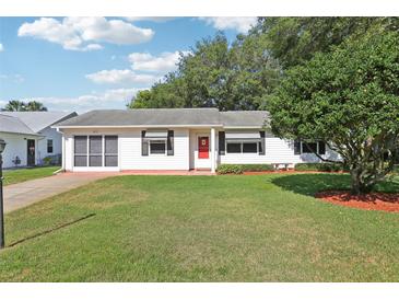 Charming single-story home with a well-manicured lawn, red door, and mature trees at 915 Sutherland Ct, Leesburg, FL 34788