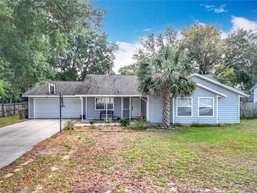 Charming single-story home with a well-manicured lawn, a palm tree, and an attached garage with a basketball hoop at 10323 Joanies Run, Leesburg, FL 34788
