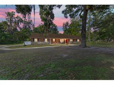 Charming home featuring a stone facade, complemented by lush landscaping and mature trees at sunset at 400 Sw 35Th St, Ocala, FL 34471