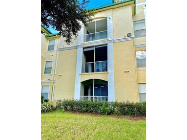 Condo exterior with screened balcony, yellow paint, and manicured landscaping at 8815 Dunes Ct # 105, Kissimmee, FL 34747