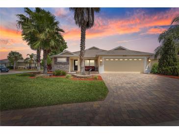 Charming single-story home with a brick-paved driveway, lush lawn, and beautiful tropical landscaping against a lovely sunset at 10460 Silver Maple Ave, Oxford, FL 34484