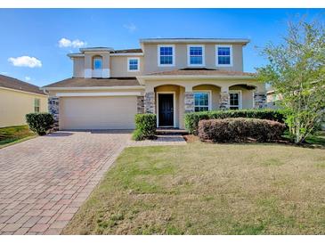 Charming two-story home featuring a brick driveway, attached garage, and inviting front porch with stone accents at 34107 Alameda Dr, Sorrento, FL 32776