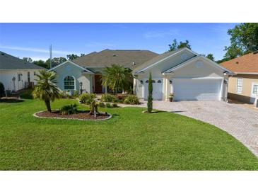 Charming two-story home with a well-manicured lawn, palm trees, and a brick-paved driveway leading to a two-car garage at 11860 Se 179Th St, Summerfield, FL 34491
