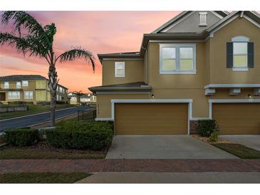 Inviting townhome featuring a two-car garage, meticulously landscaped yard, and a lush palm tree at 17519 Promenade Dr, Clermont, FL 34711