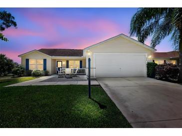 Charming single-story home with a well-manicured lawn, inviting patio, and two-car garage, set against a colorful sunset sky at 2290 Due West Dr, The Villages, FL 32162