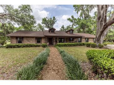 Charming single-story brick home with a well-manicured lawn, mature trees, and a inviting walkway at 12196 Ne 4Th Pl, Oxford, FL 34484
